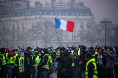 Demonstrators gather near the Arc de Triomphe as a French flag floats during a protest of Yellow vests (Gilets jaunes) against rising oil prices and living costs, on December 1, 2018 in Paris. - Anti-government protesters torched dozens of cars and set fire to storefronts during daylong clashes with riot police across central Paris on December 1, as thousands took part in fresh "yellow vest" protests against high fuel taxes. (Photo by - / AFP)